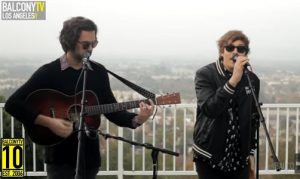 Two men singing into microphones on a rooftop.