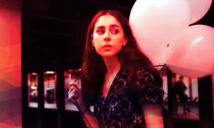 A girl holding balloons in a dark room for a music video.