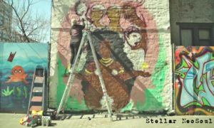 A man on a ladder painting a mural on the building.