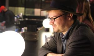 A man in a hat sitting at a bar in color image.