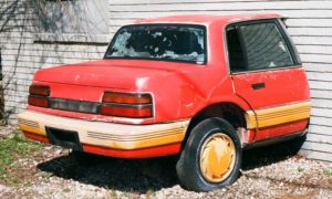 A red and yellow car is parked in front of a house.